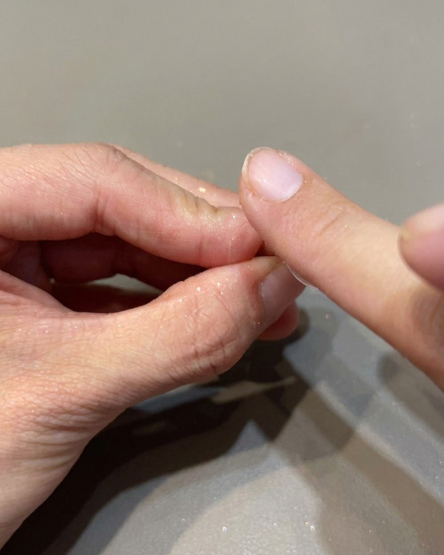 A small sponge applicator rubbing iridescent mirror powder onto a nail to create a high-shine finish.