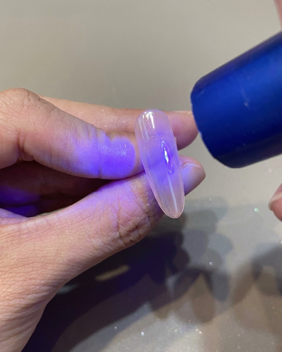 A nail brush applying a clear, glossy top coat over a manicured nail.