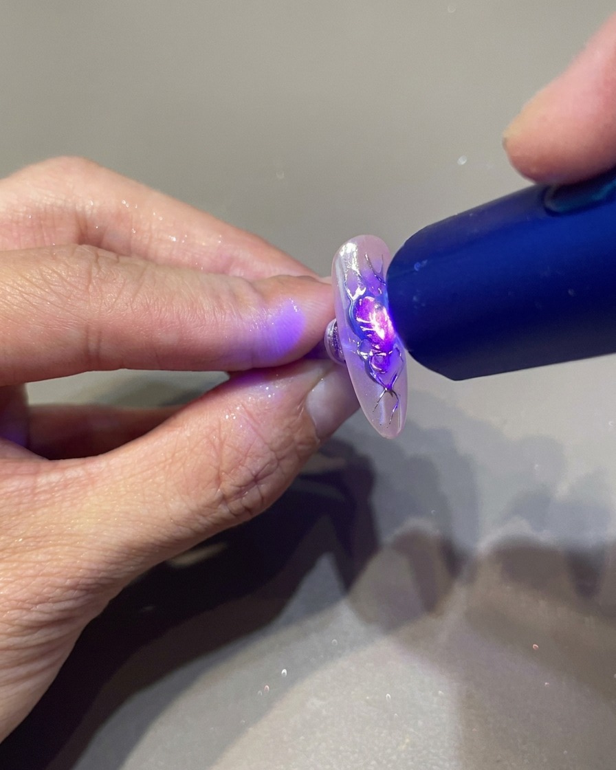 A portable UV lamp held over a manicured nail to set the clear 3D gel details on a flame-decorated heart design.