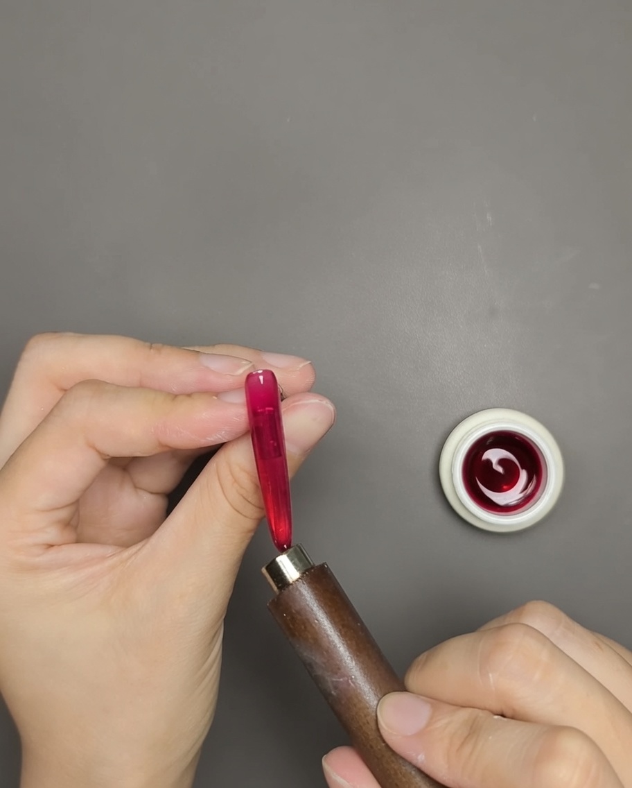 A hand using a bar magnet held near a red cat eye gel nail to reveal the magnetic shimmer line.