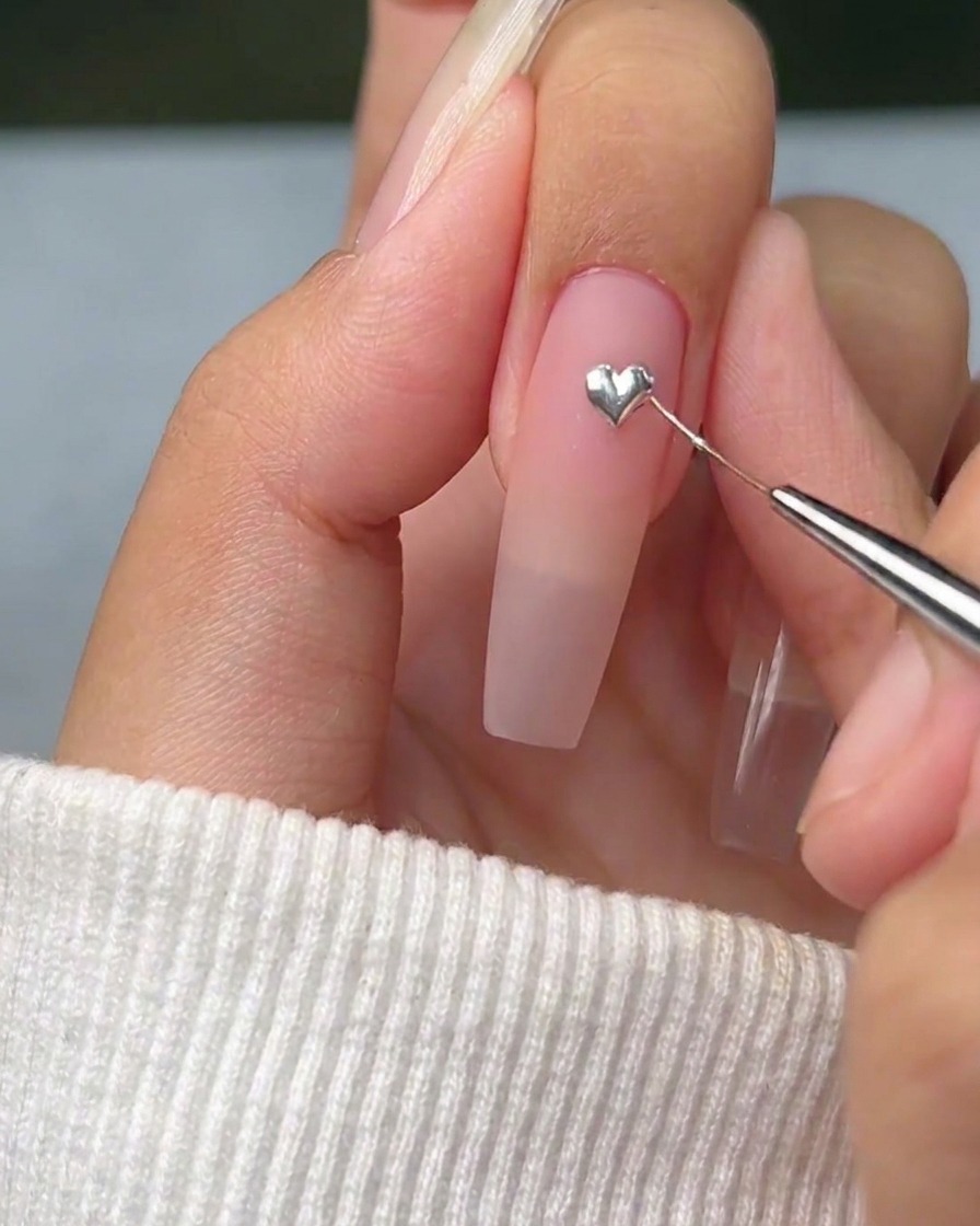 A fine liner brush carefully pulling the edges of a silver gel dot into a sharp, defined heart shape on the nail.