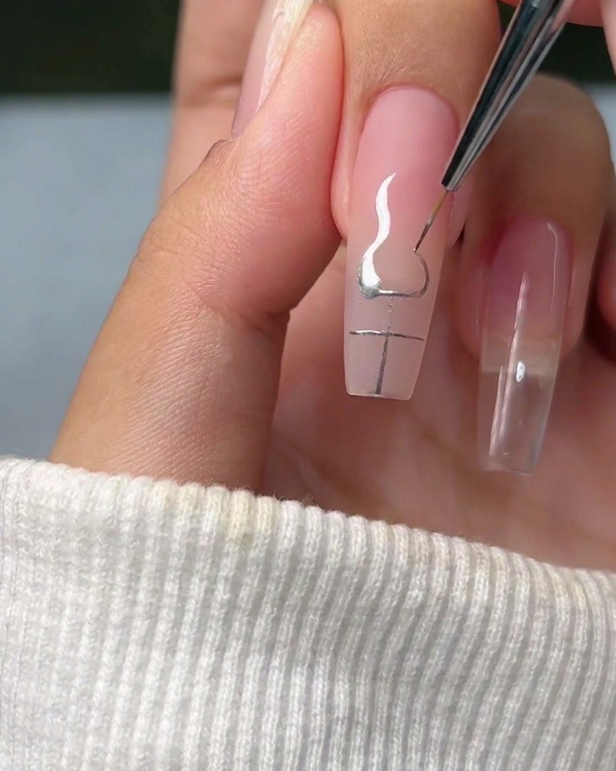 A liner brush tracing elegant, flame-like curves originating from the corners of a silver cross on a fingernail.