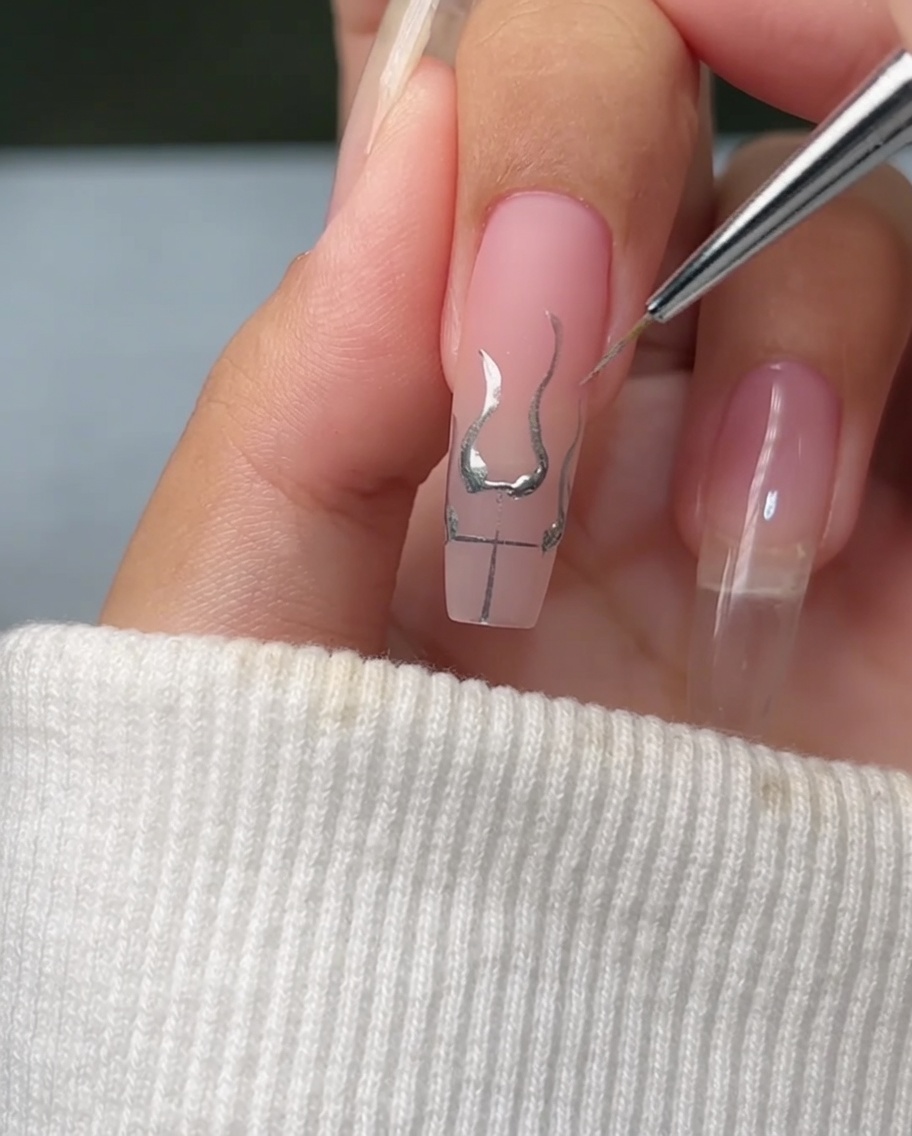 A fine brush filling the base of flame outlines on a nail with bright, reflective metallic silver gel.