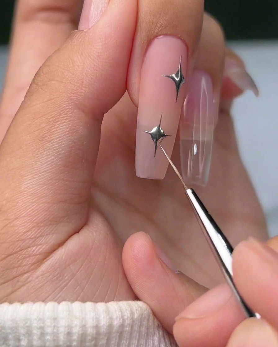 A finished nail design featuring a metallic silver four-pointed star and a small silver gem accent.