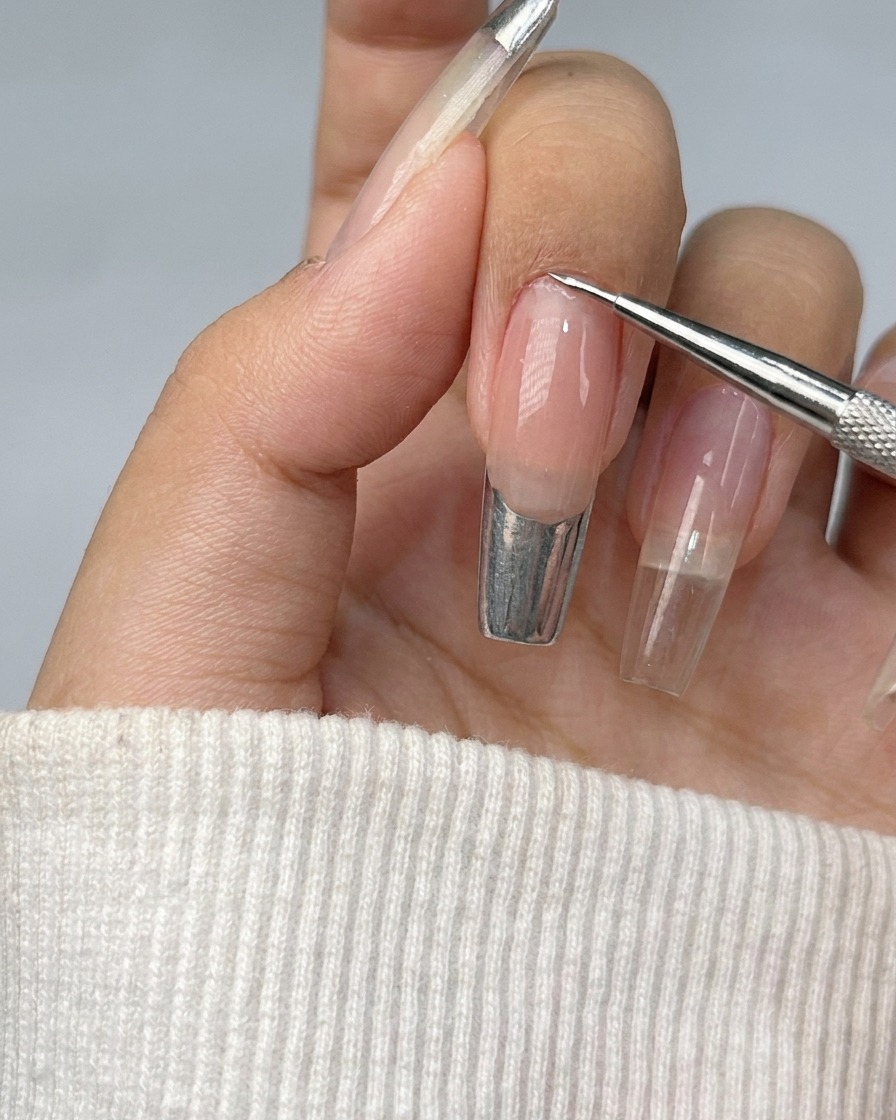 A nail with a French tip being filled in with shiny silver metallic gel.