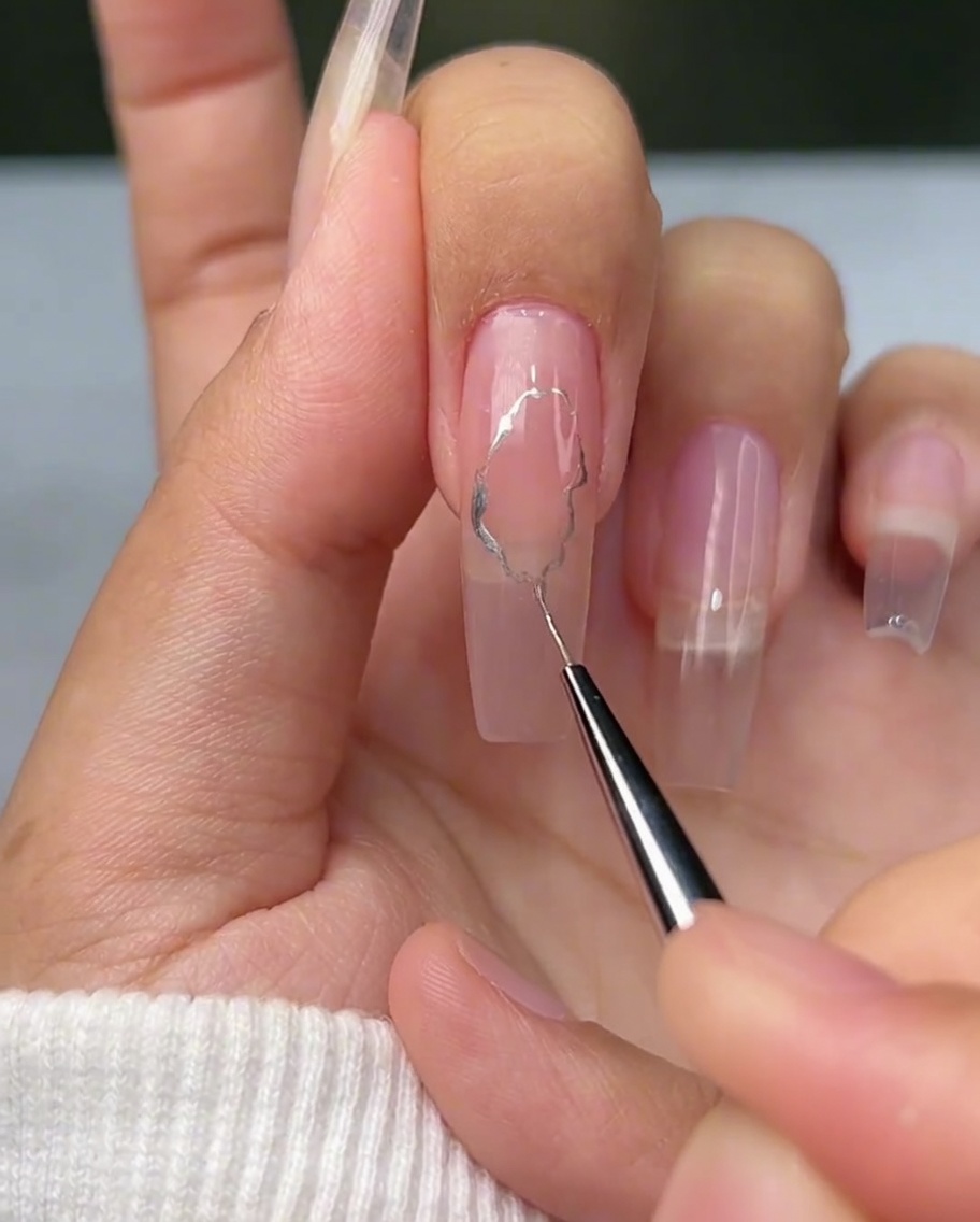 A fine liner brush drawing irregular, wavy silver lines on a nail.