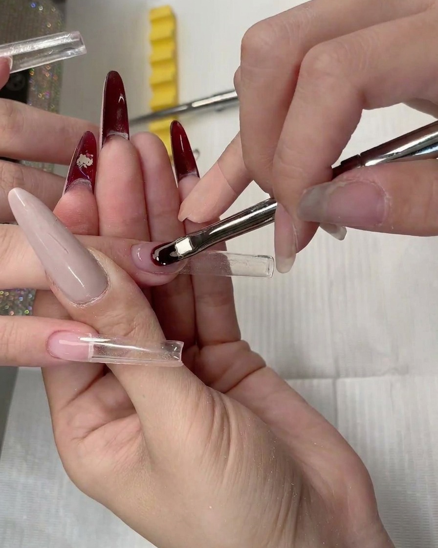 A close-up of a clear nail extension form being positioned under the natural nail plate.