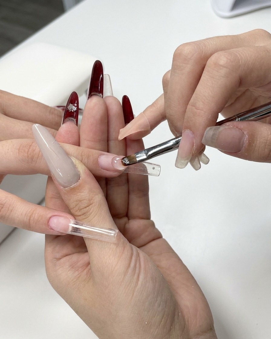 A close-up of a gel brush applying clear builder gel onto a clear nail extension form.