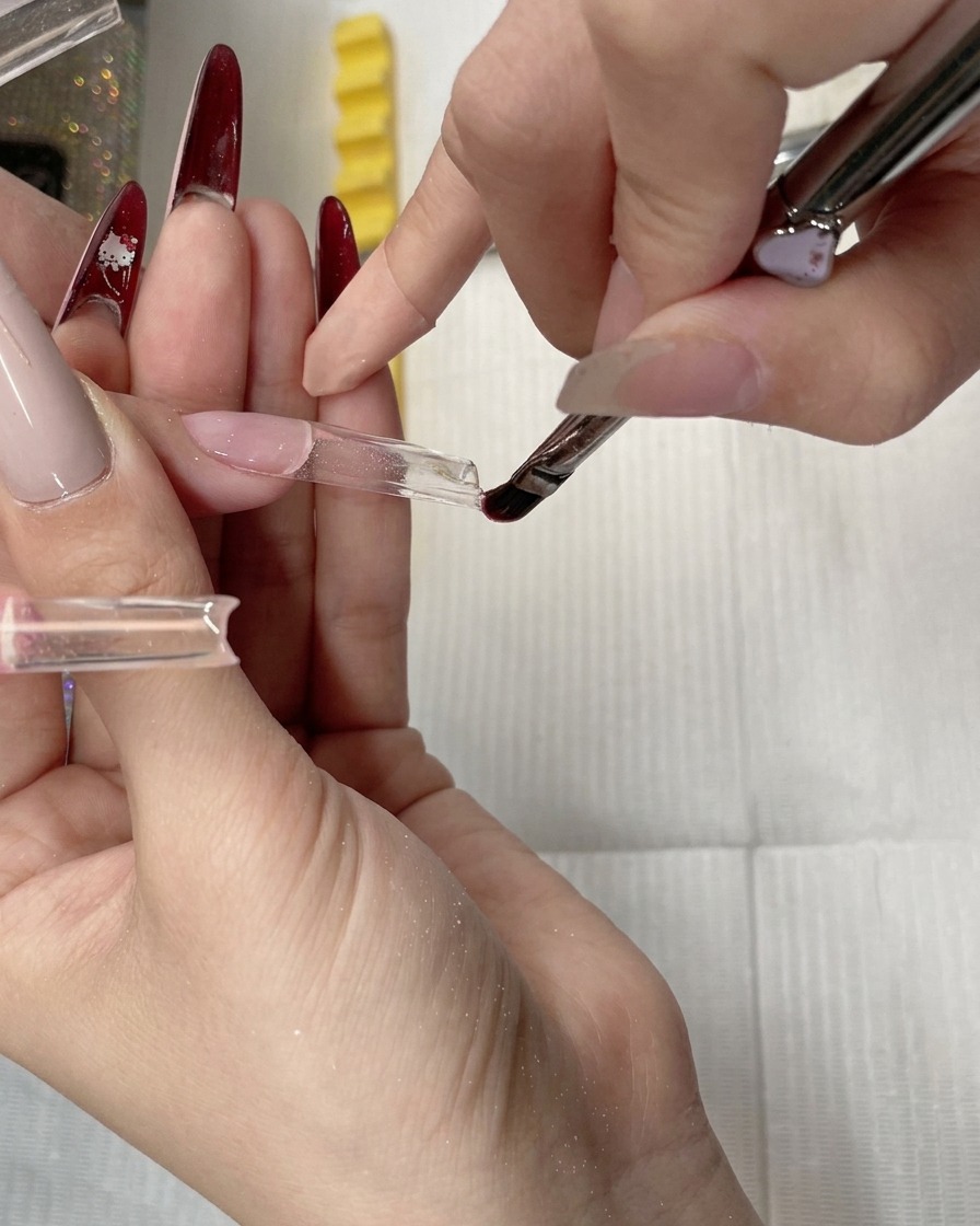 A gel brush smoothing and leveling clear builder gel along the tip of a clear nail form.