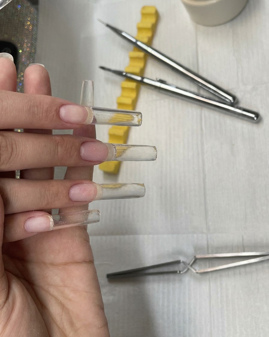 Four fully built, uncured clear extra-long square gel nail extensions on a hand before the filing step.