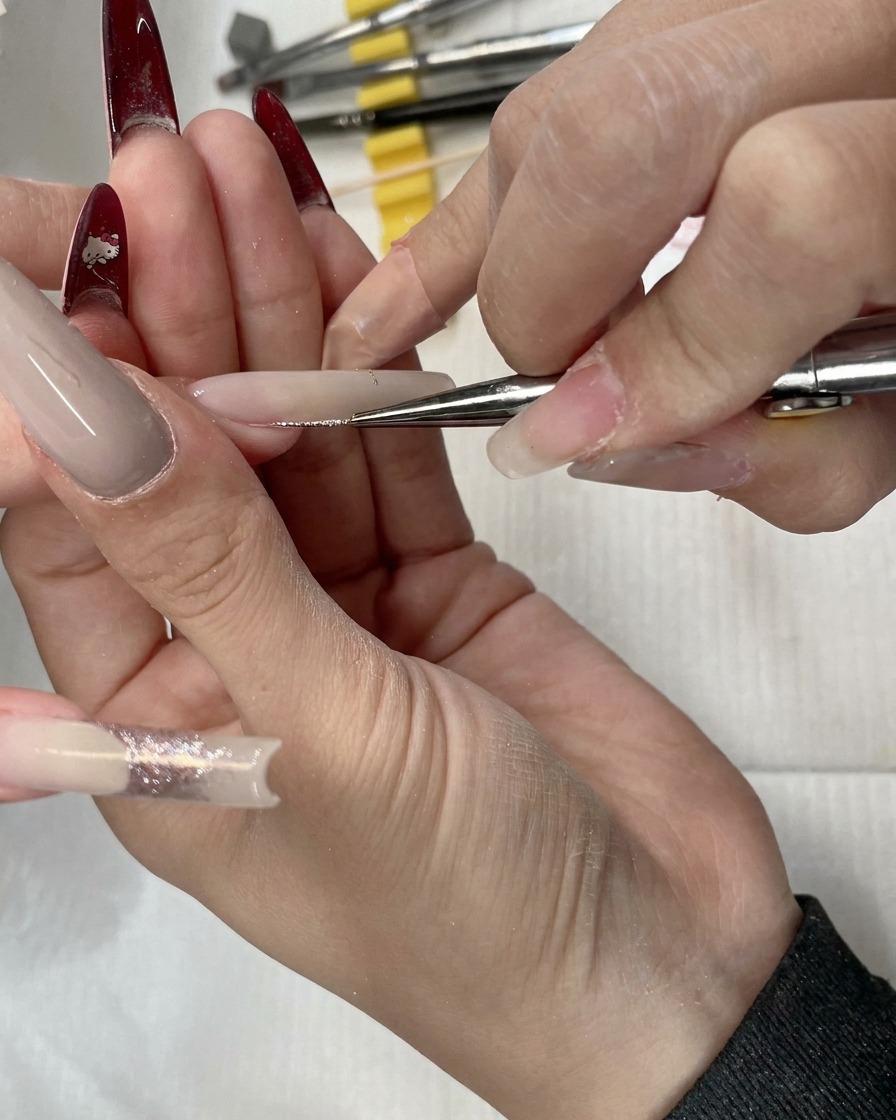 A close-up of a liner brush applying rose gold glitter across the nail bed.