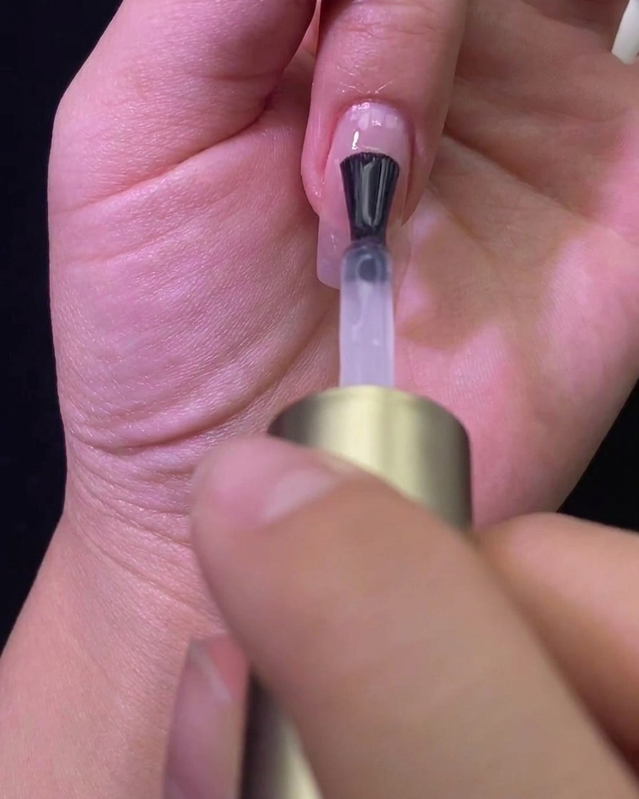 A brush applying a matte top coat over a nude-colored nail, transforming the finish.