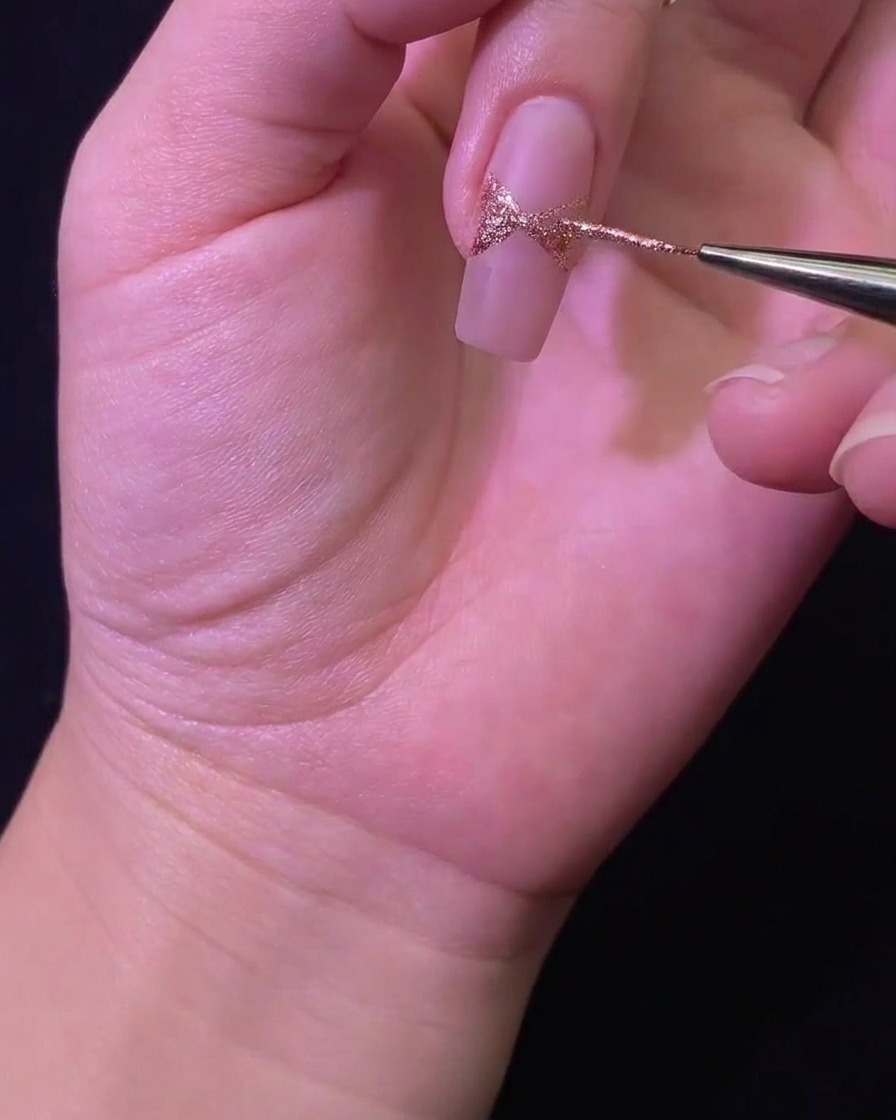 A close-up of a liner brush filling in the glitter bow shape on the nail surface.