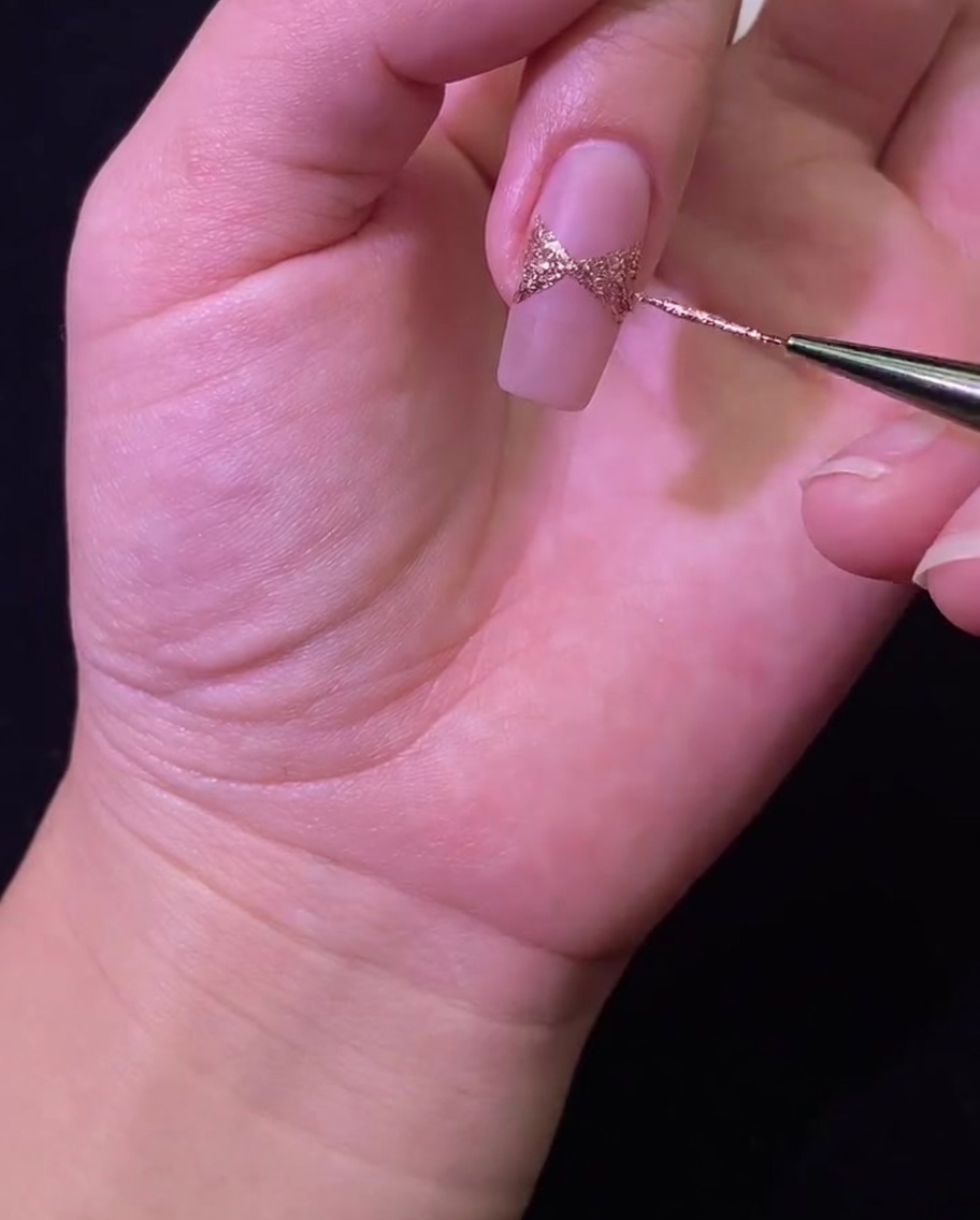A nail positioned under a UV/LED lamp for curing the rose gold glitter bow nail art.