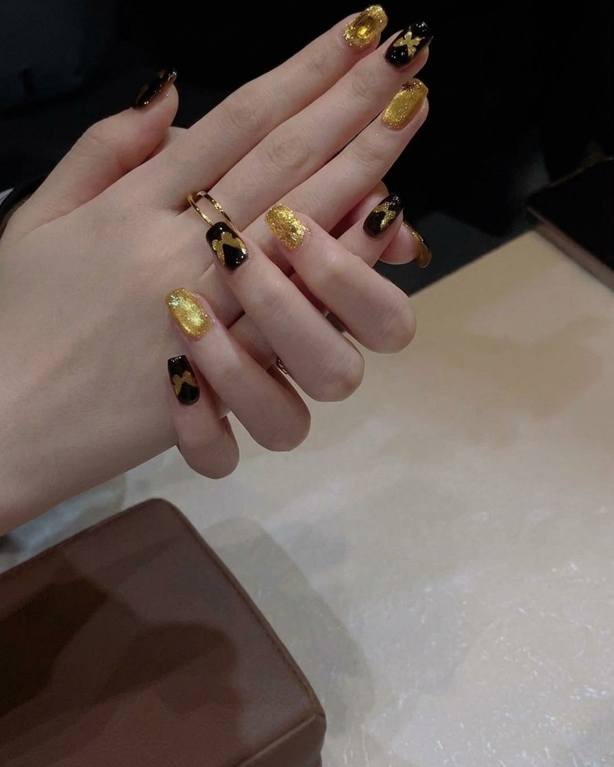 A gel brush applying a layer of shimmery gold cat-eye polish onto a black-painted nail.