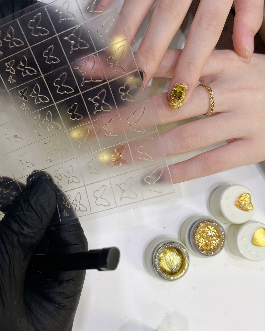 Fine-tipped tweezers holding a delicate hollow butterfly sticker peeled from a clear sheet.