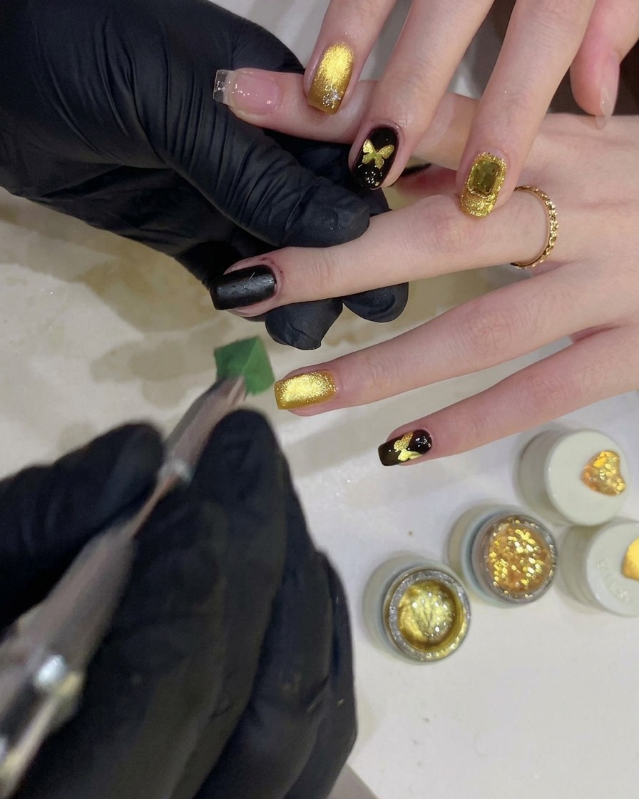 A person using a sponge tool to dab black gel over a butterfly-shaped stencil on a fingernail.
