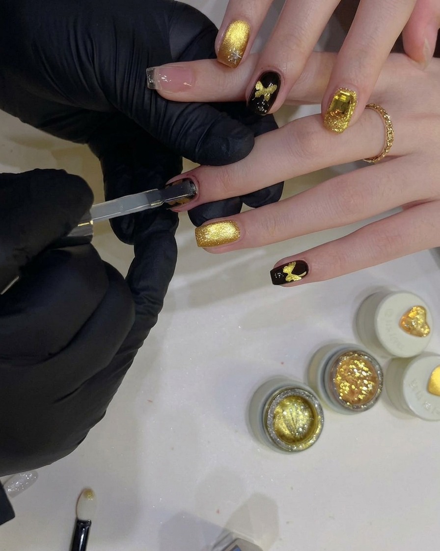 A flat gel brush applying a clear, glossy top coat over a black nail with a sparkling gold butterfly design.