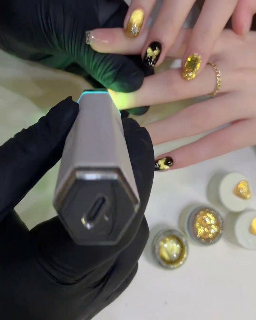 A handheld UV/LED lamp positioned over a finished nail design to cure the final clear top coat.