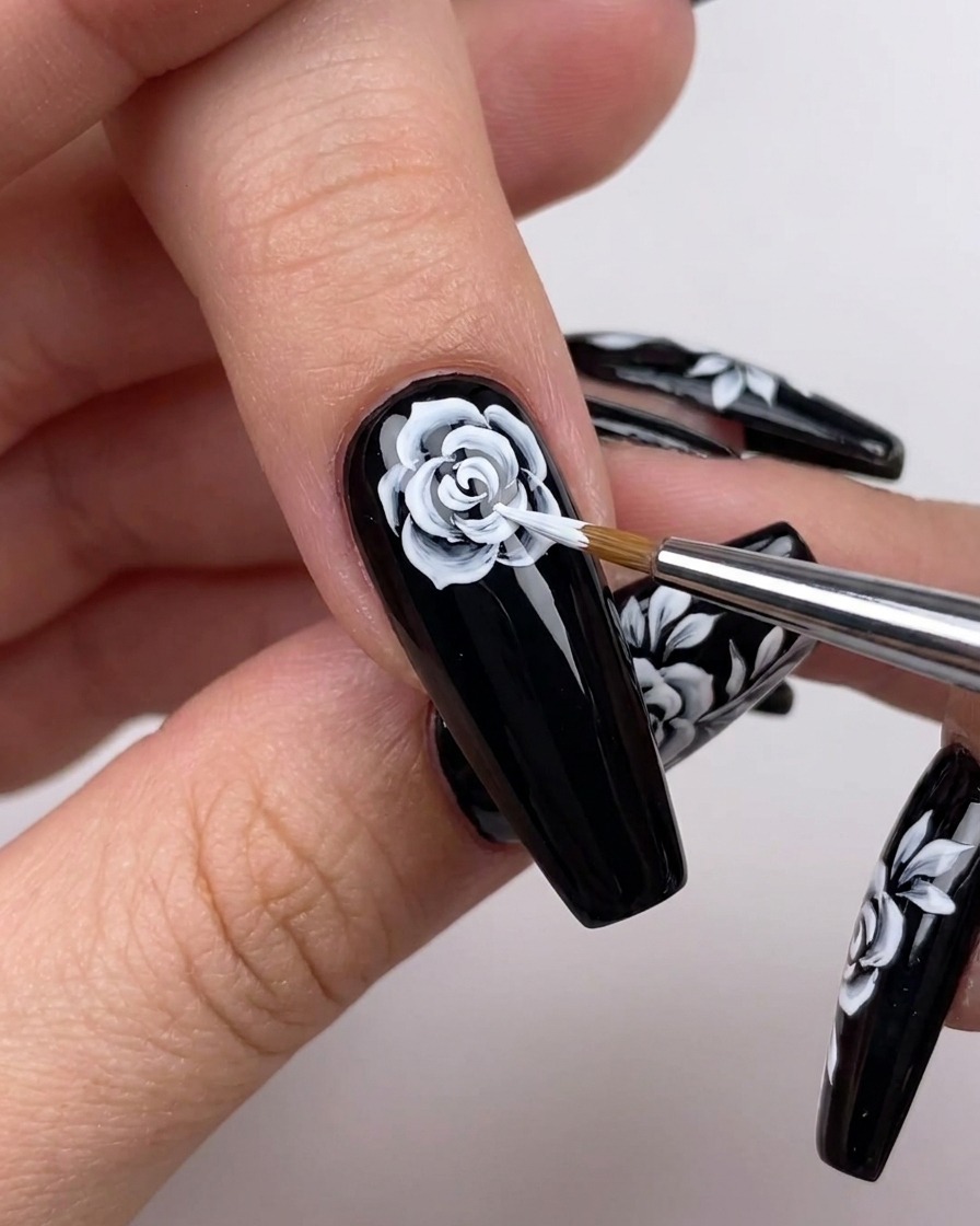 A detailed close-up of a hand using a fine brush to extend white petal lines outwards from the center of a floral nail art design.