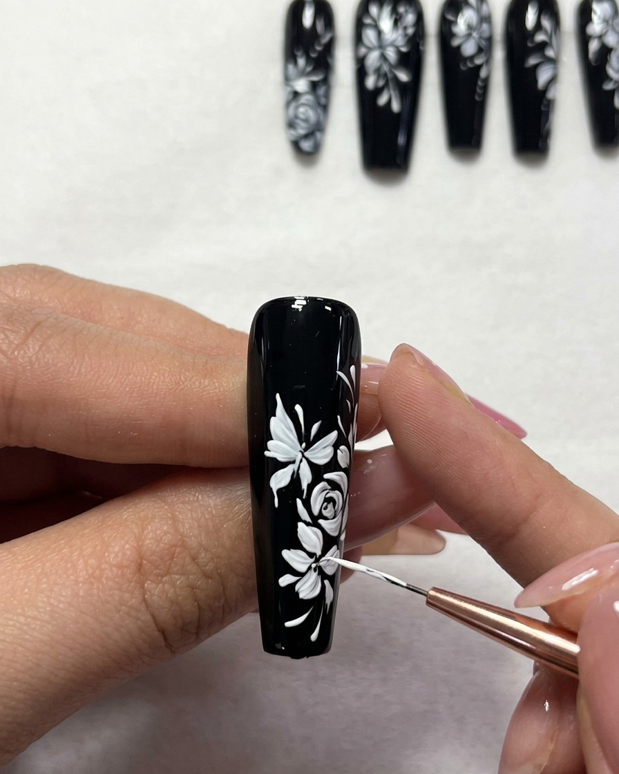 Close-up of a detail brush adding small white dots to a floral nail art design on a black base.