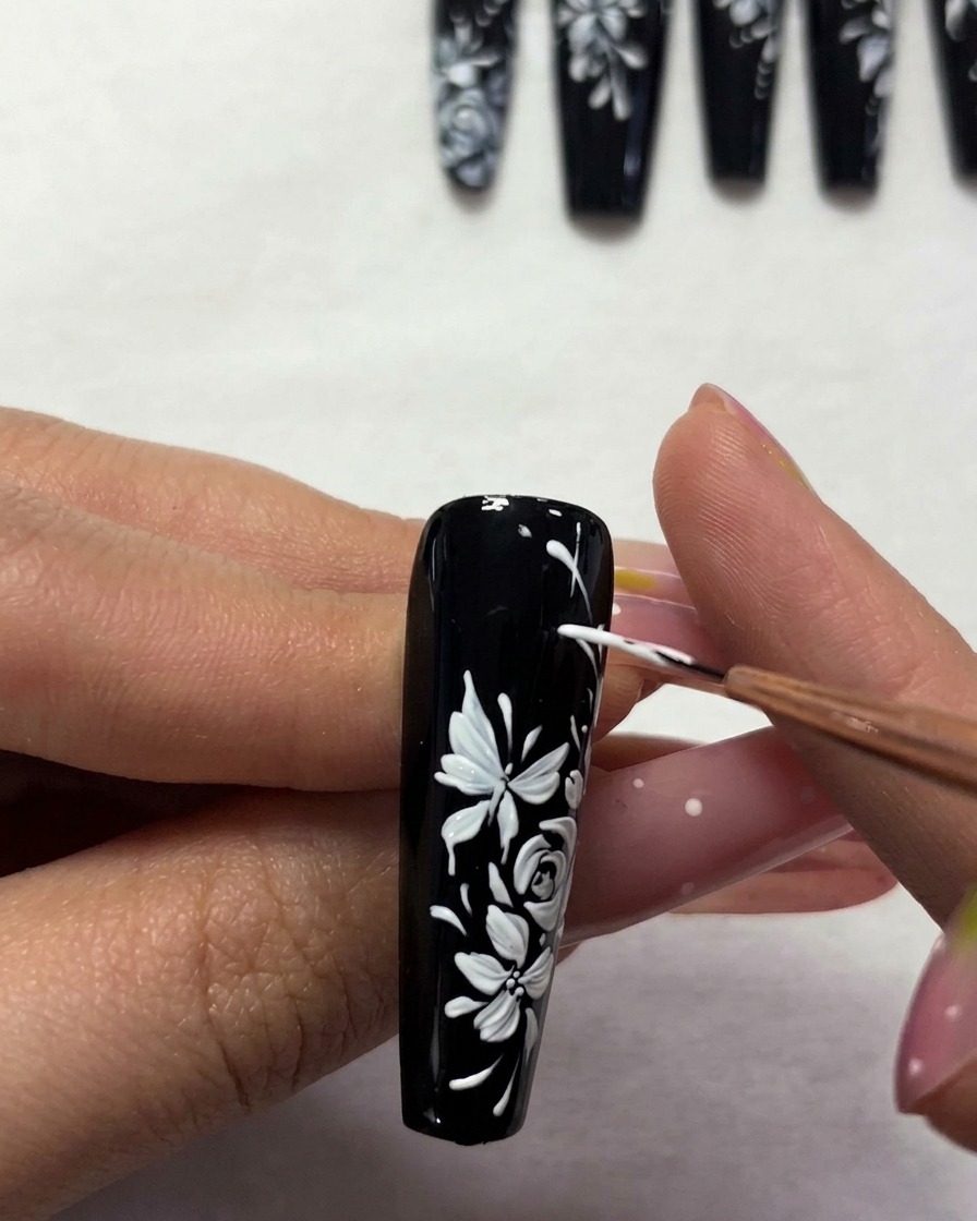 A brush applying a clear top coat over the finished floral nail art.
