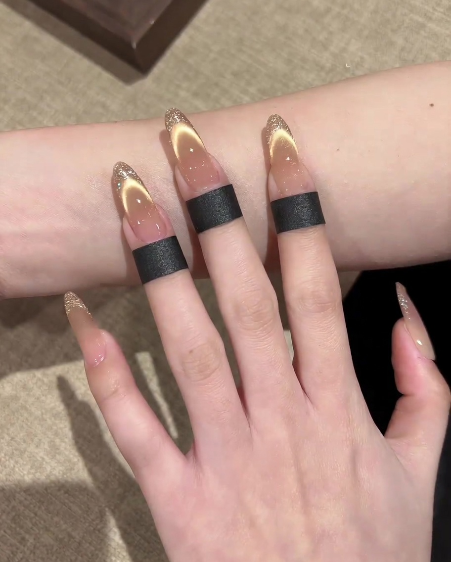A brush applying a shimmering gold magnetic cat-eye gel onto the nail.