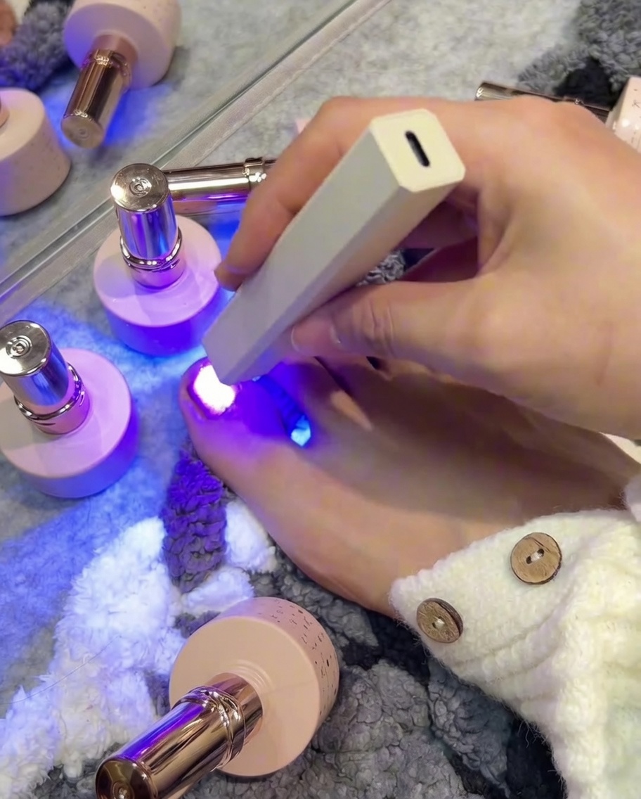 A nail brush applying rose pink cat-eye gel polish to a smaller toenail.