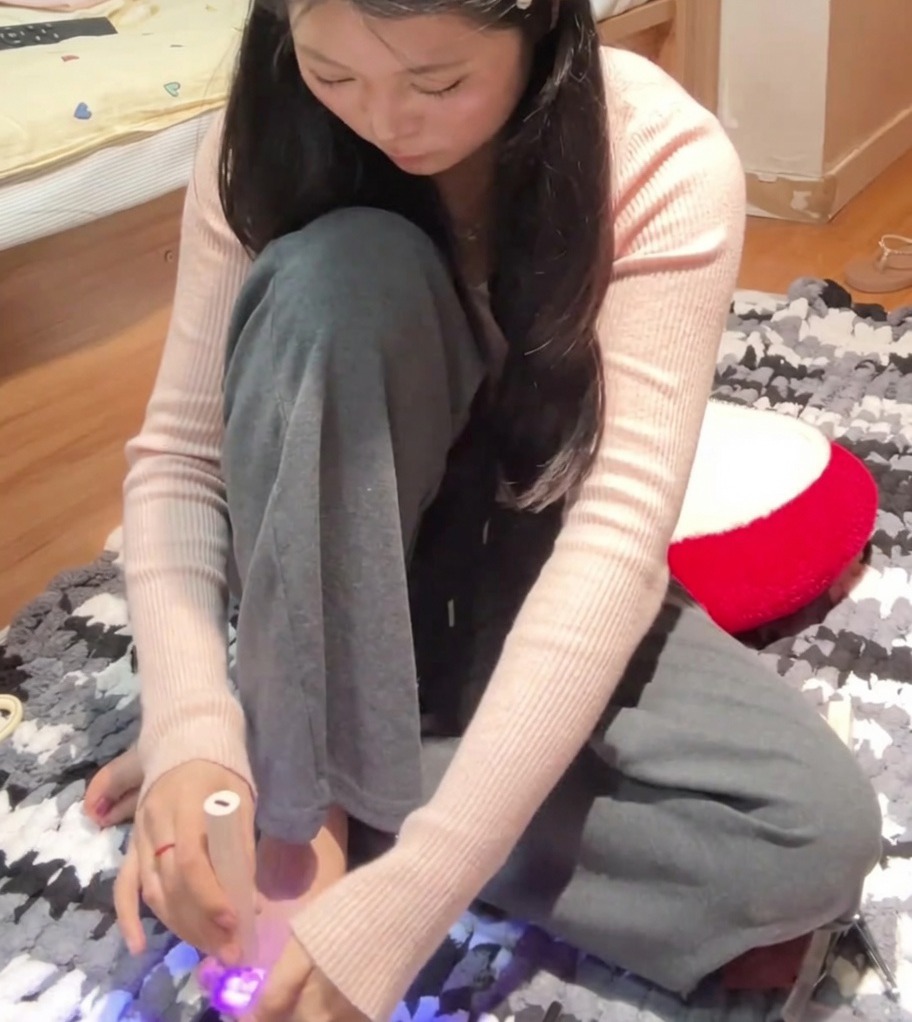 A person using a handheld UV lamp to cure the big toenail on their left foot after applying rose pink magnetic gel polish.