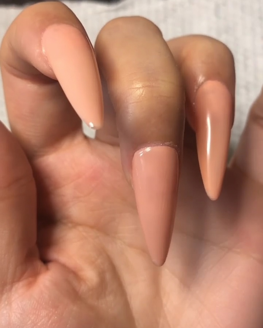 A nail brush applying a thin layer of top coat over the nude gel on the index finger.