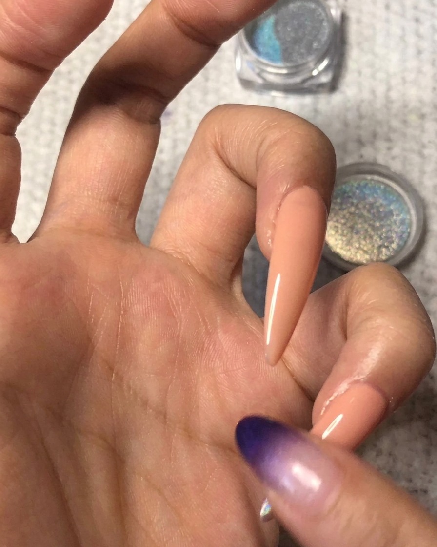 A clean fingertip gently blending the edge of the holographic powder upwards over the nude nail to create a seamless ombre gradient.