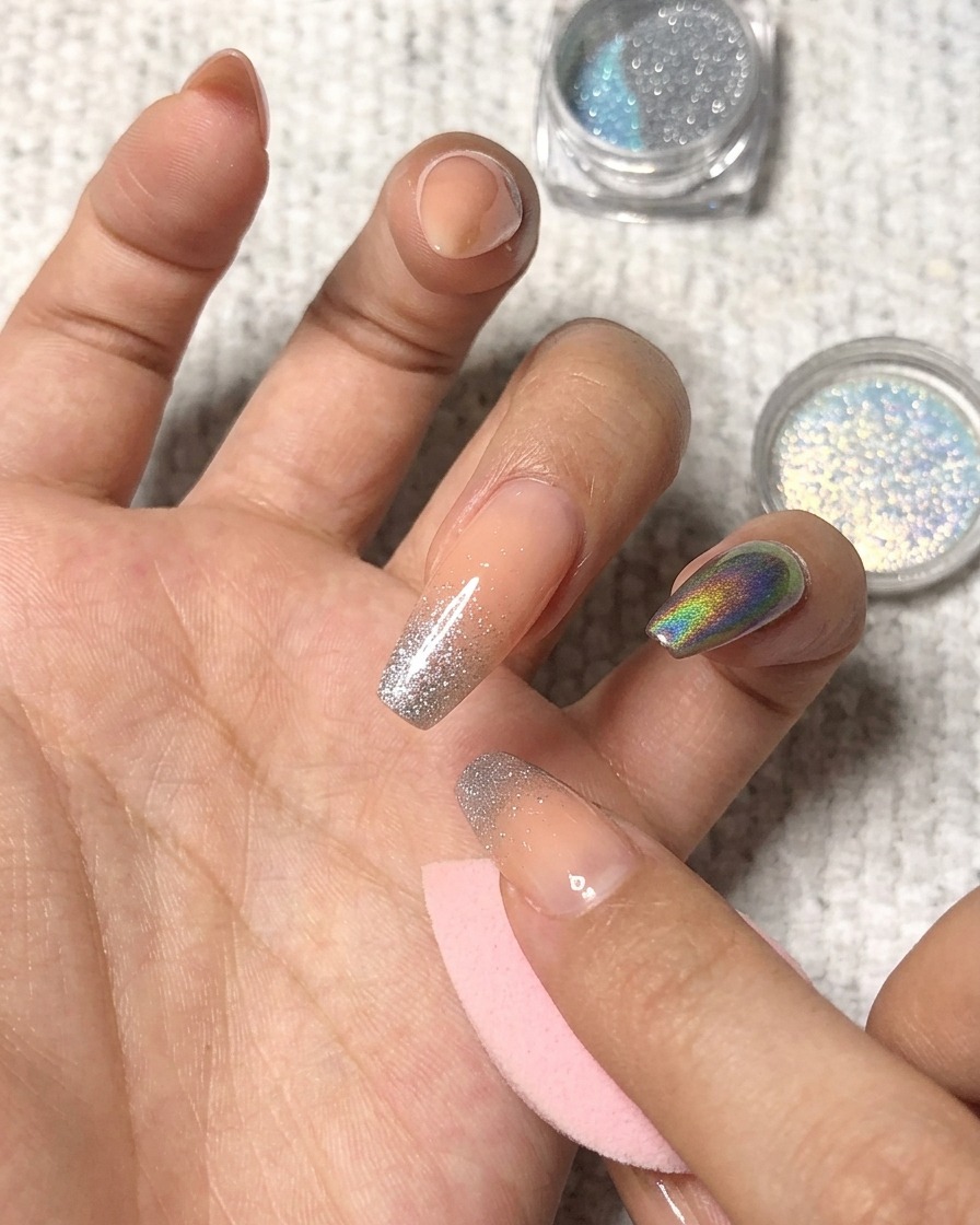 Dabbing holographic powder onto the tip of a manicured ring finger.