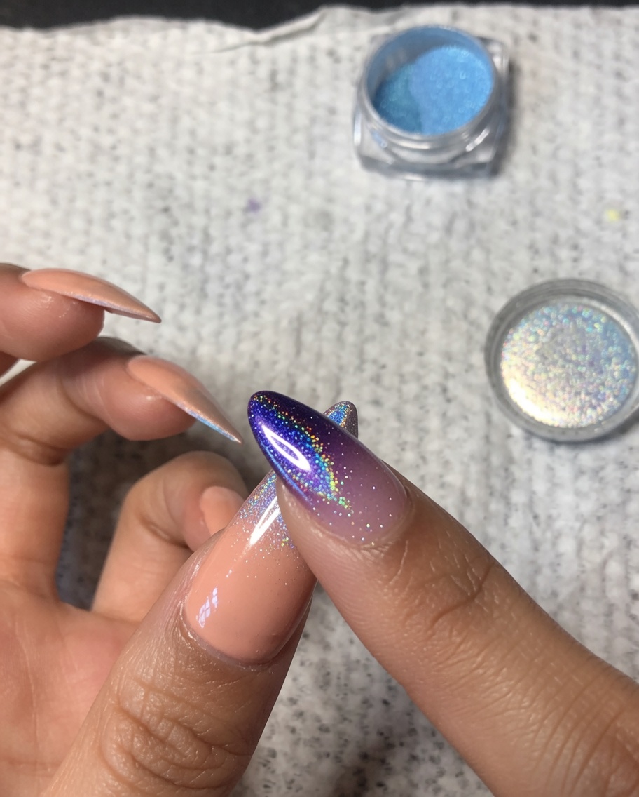 A close-up of a finger gently blending holographic chrome powder over the middle of a thumbnail to create a soft ombre fade.