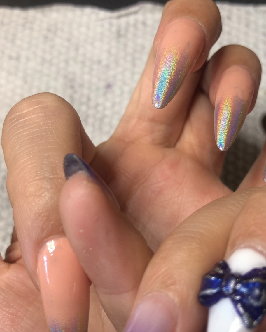 A close-up of a brush applying a clear gel layer over an index finger with a holographic chrome ombre gradient.