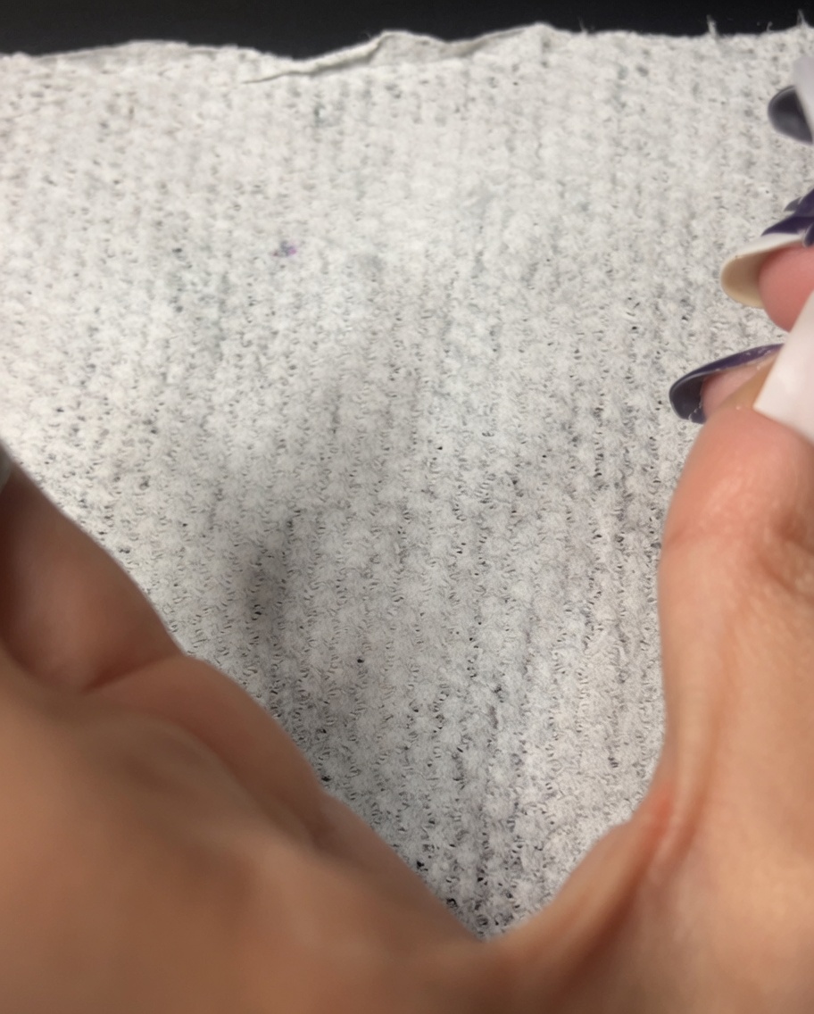 A lint-free wipe being used to clean the surface of a manicured fingernail.