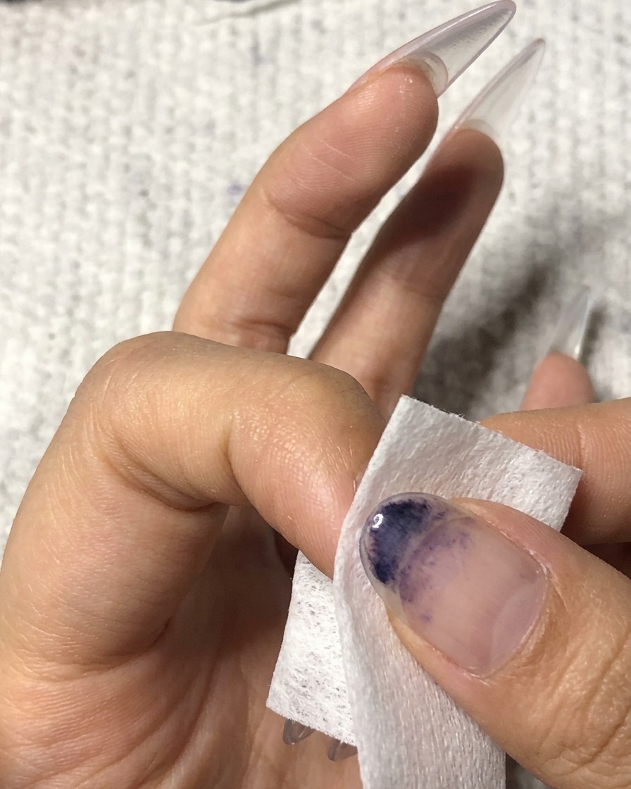 A lint-free wipe being used to clean the surface of a manicured ring fingernail.