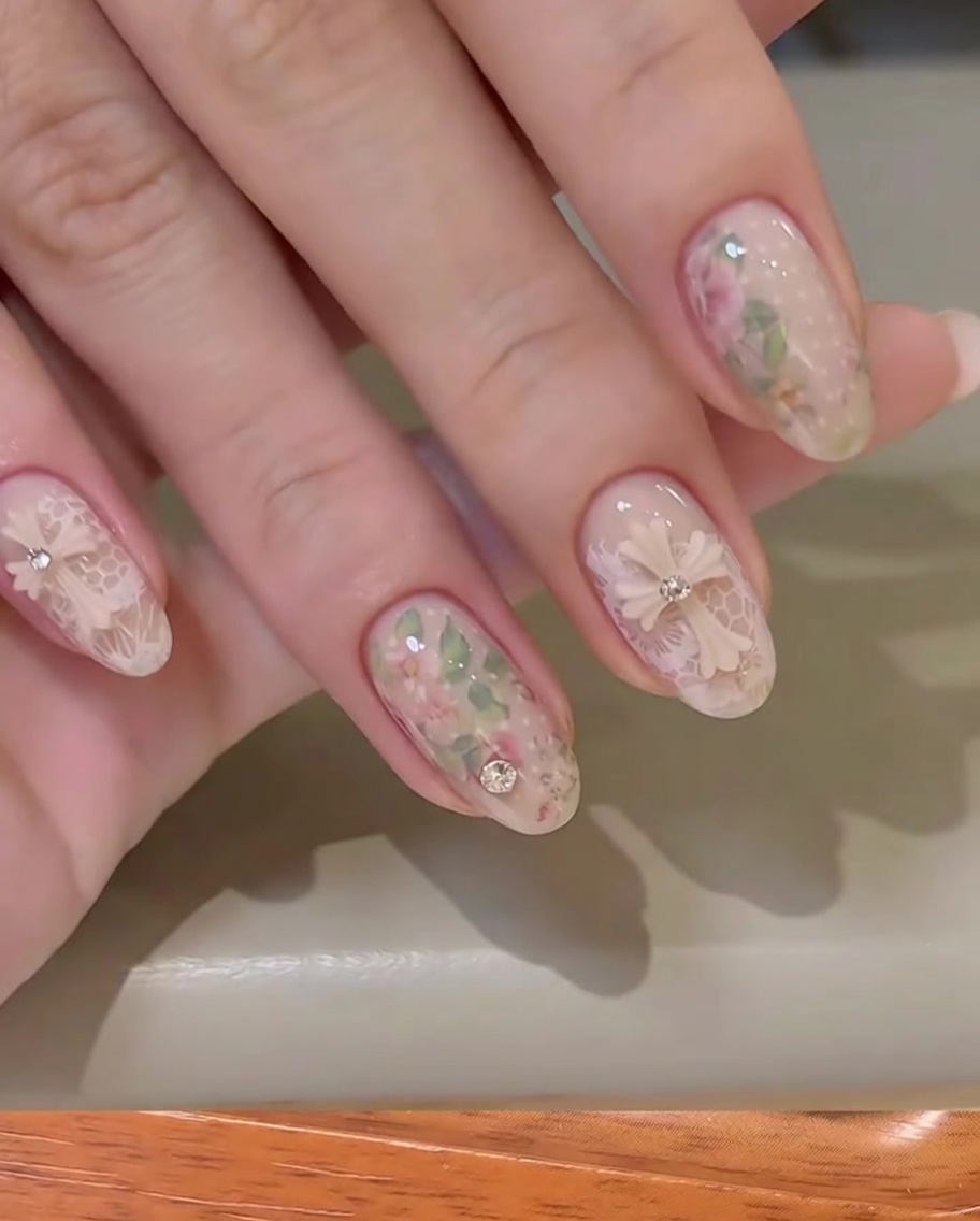 A piece of floral transfer foil being pressed onto a nail surface with a finger.