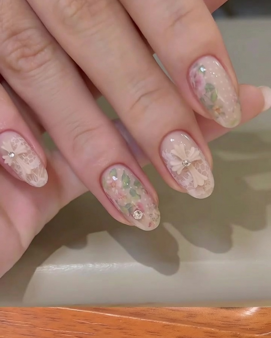 Close-up of a hand peeling away a thin floral transfer foil backing from a nude-colored fingernail.