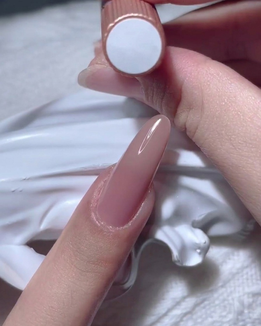 A hand holding up a bottle of nude gel polish.