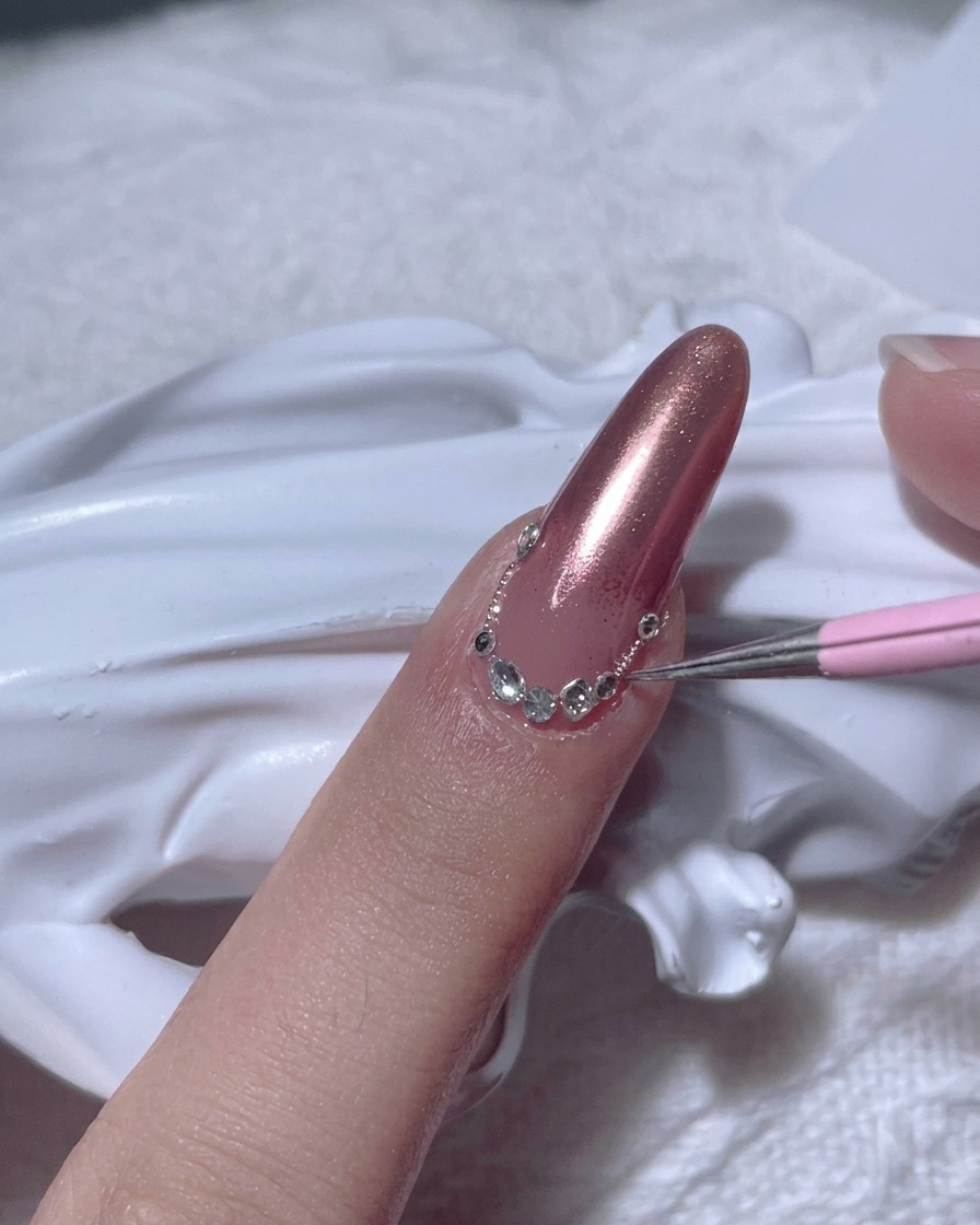 A detailer tool placing a clear rhinestone on the nail near the cuticle.