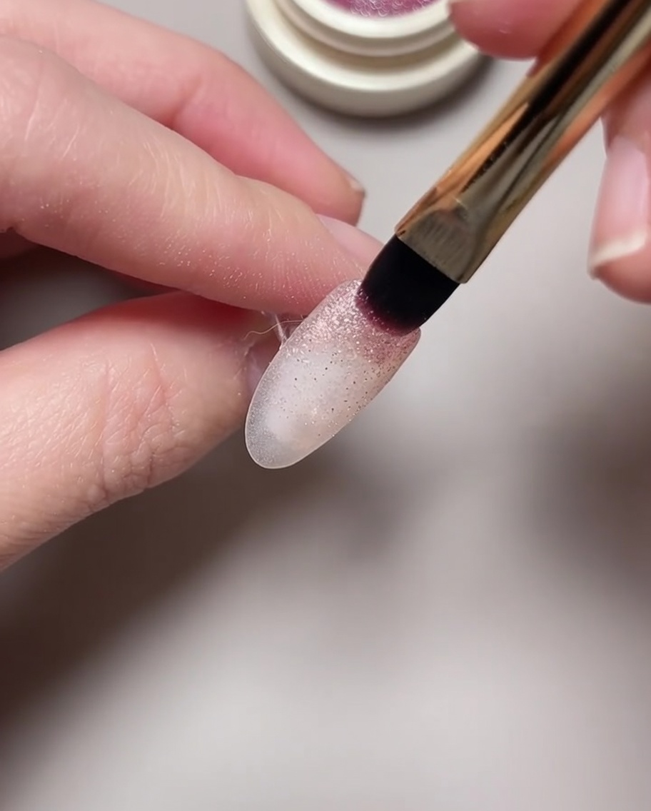 A close-up of a magnet tool being hovered over a wet cat eye gel polish to form a nebula pattern.