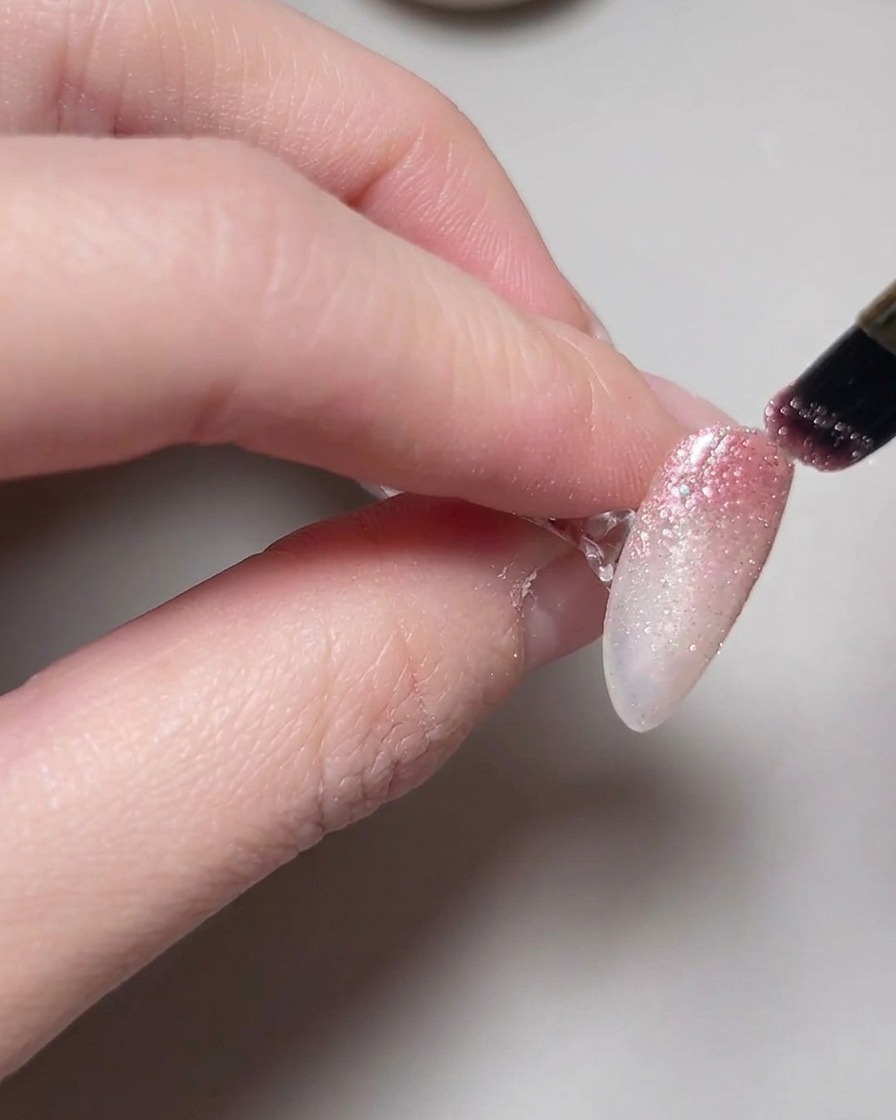 A hand positioned inside a lamp with cat eye gel polish curing on the nails.
