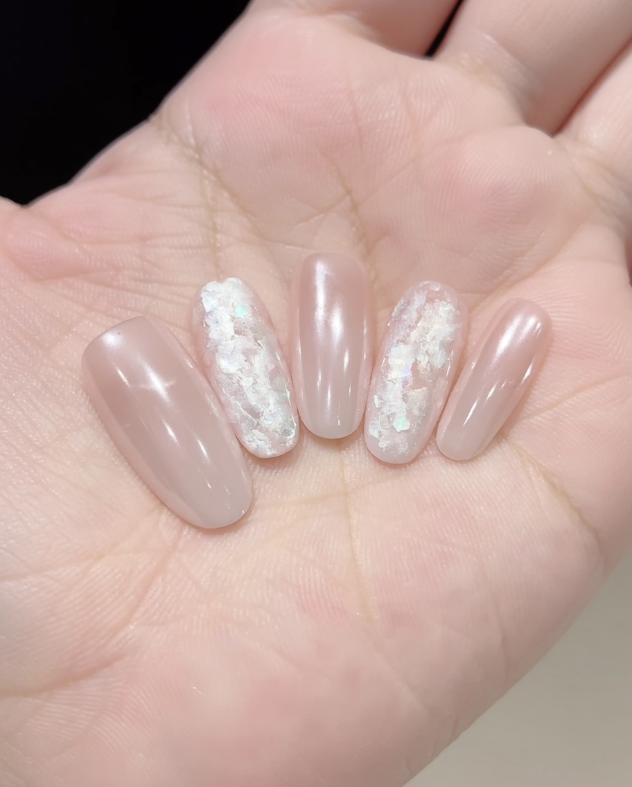 A pair of tweezers or a brush placing iridescent shell flakes onto a gel-coated nail.