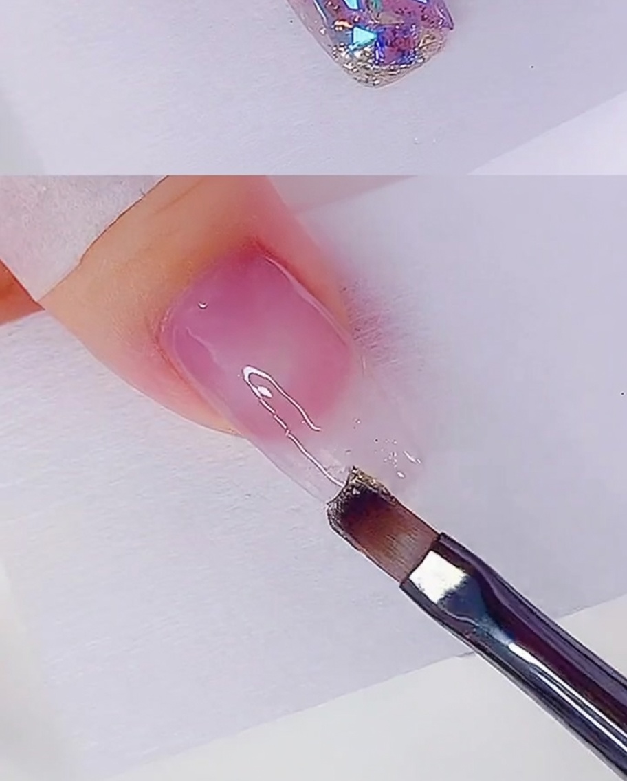 A flat brush applying a thin layer of rose gold glitter gel to the tip of a nail.