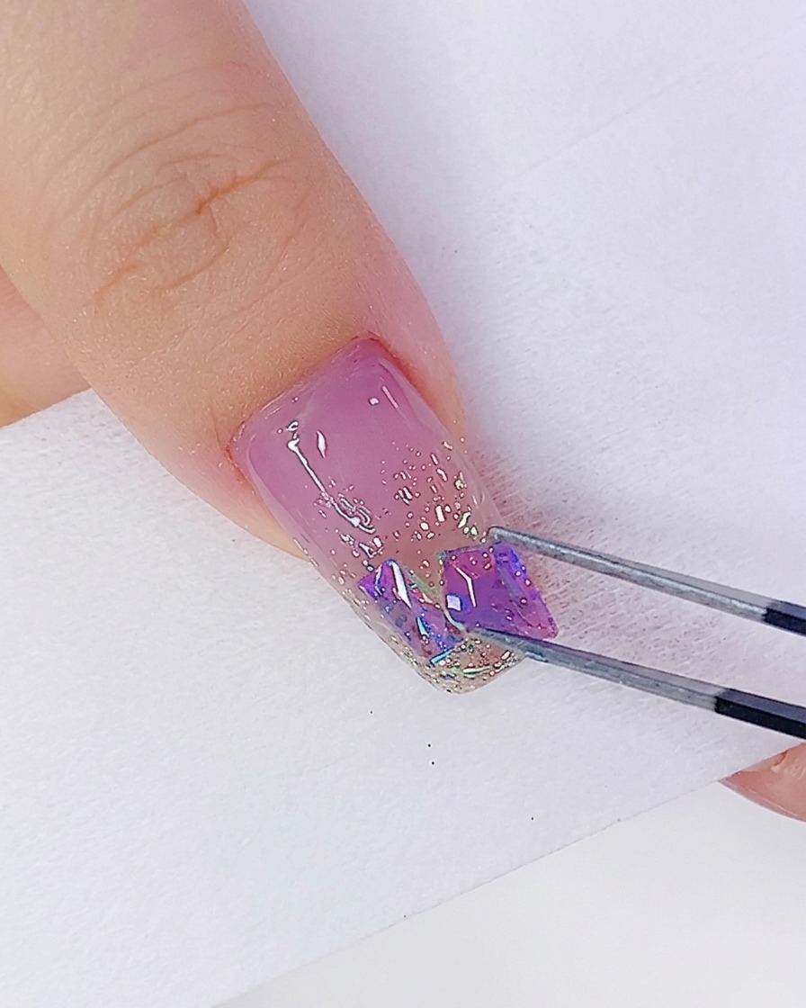 A cluster of assorted geometric iridescent rhinestones being arranged on the nail.