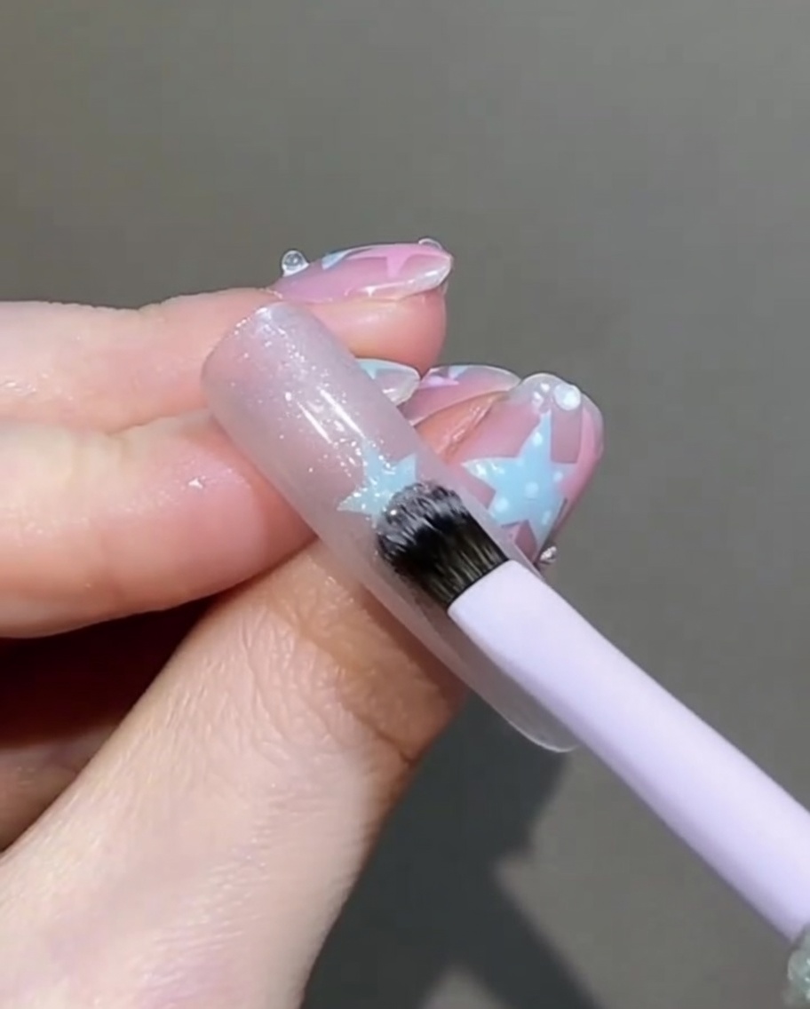 A small flat brush gently tapping and smoothing the surface of the wet cat-eye gel on the nail.