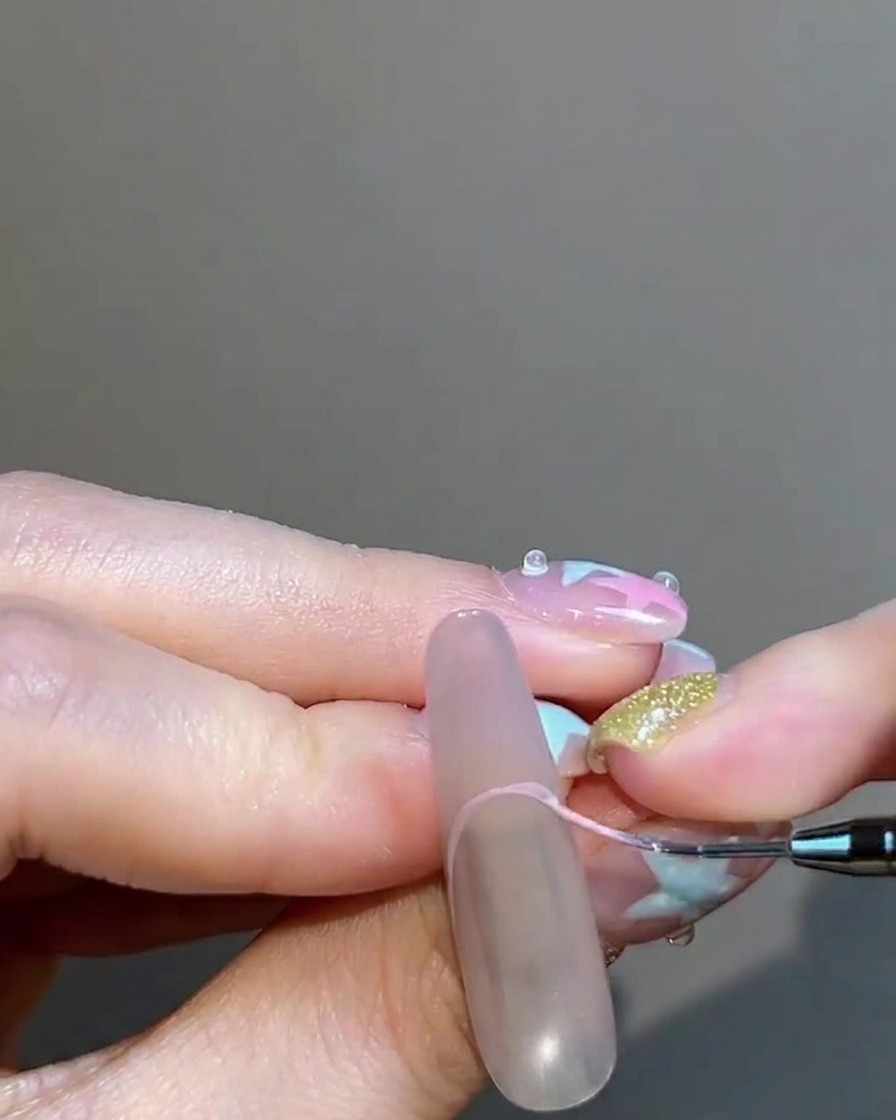 A fine liner brush carefully painting a pinkish-nude gel French tip on the nail.