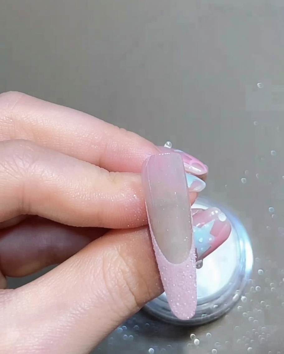 A soft brush sweeping over a manicured nail to remove excess loose glitter powder, showing a clean French tip.