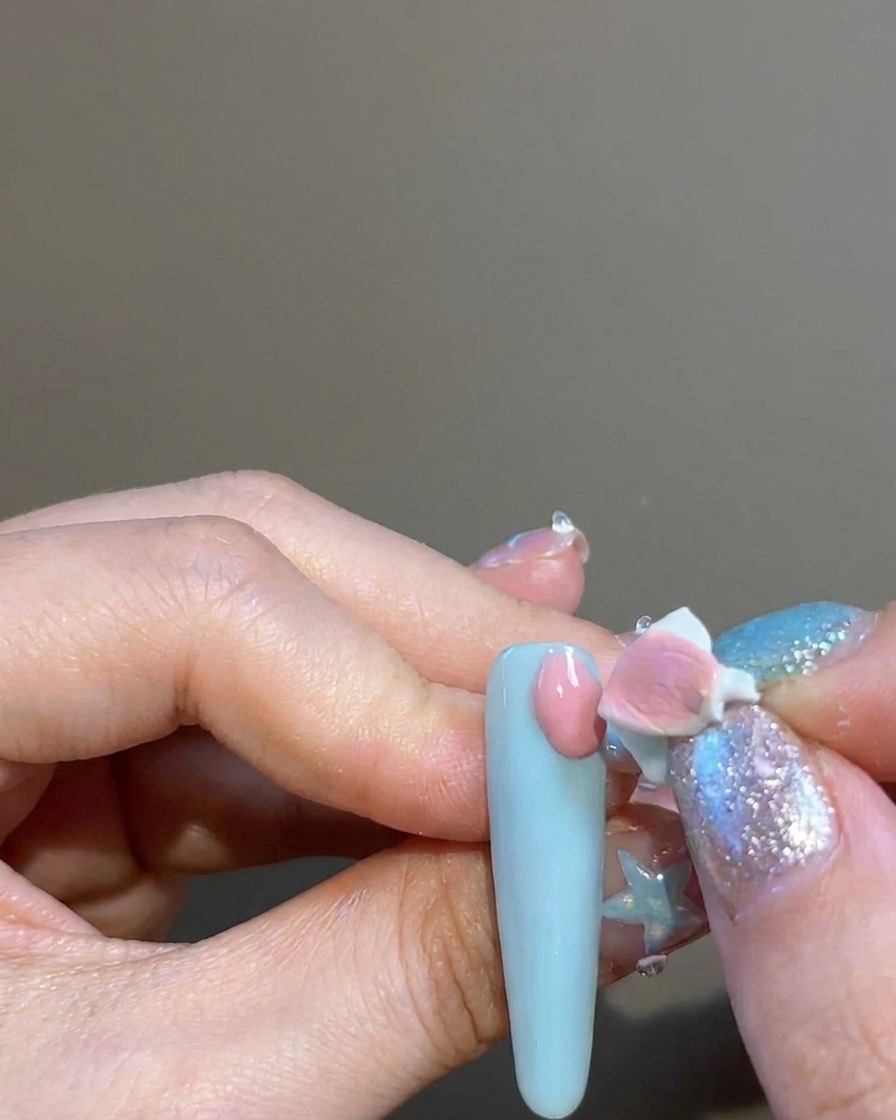 A finger using a small sponge tip to dab pink pigment onto the nail around a cross-shaped sticker.