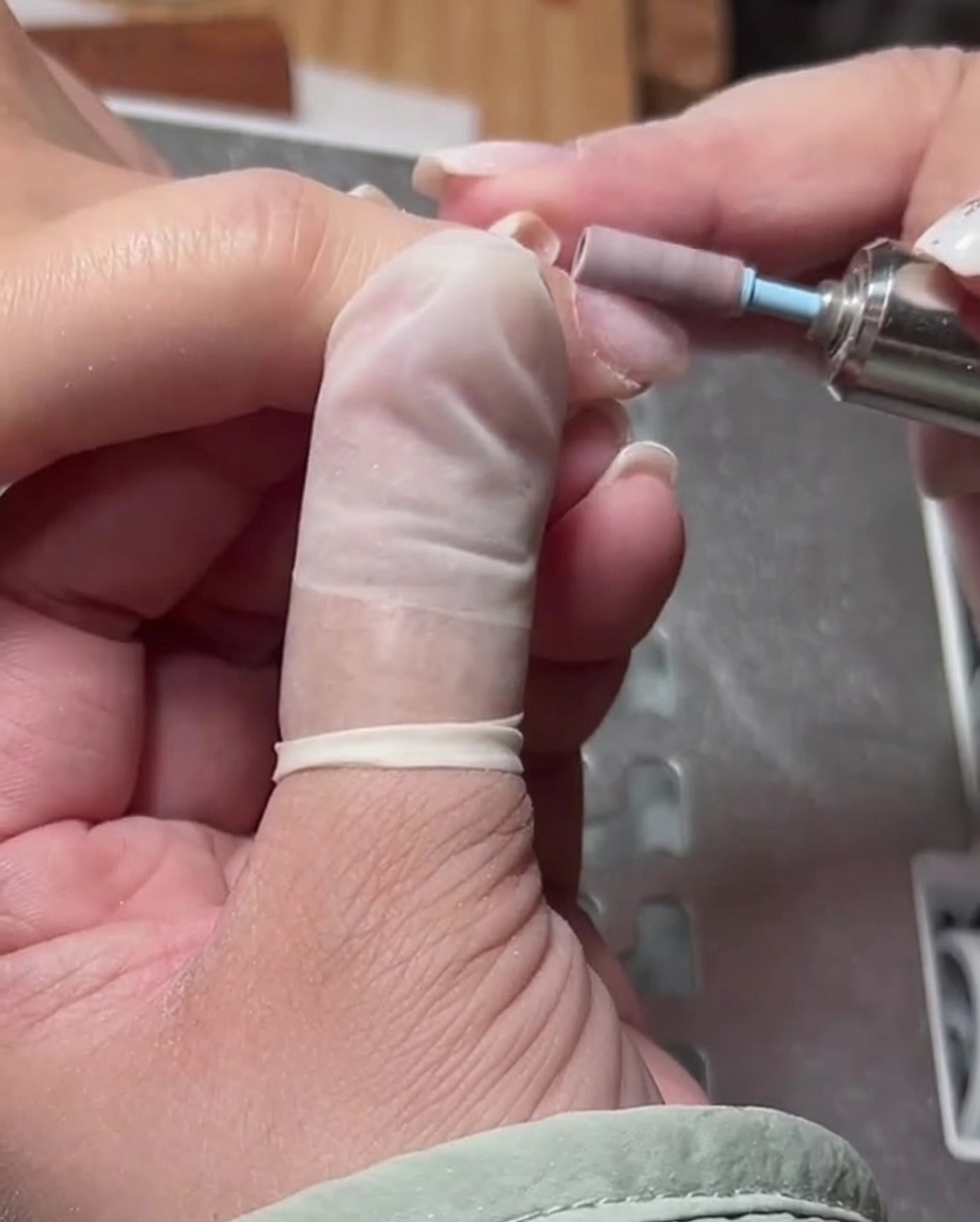 A close-up view of a cylindrical e-file bit being used to smooth the skin around the cuticle area.